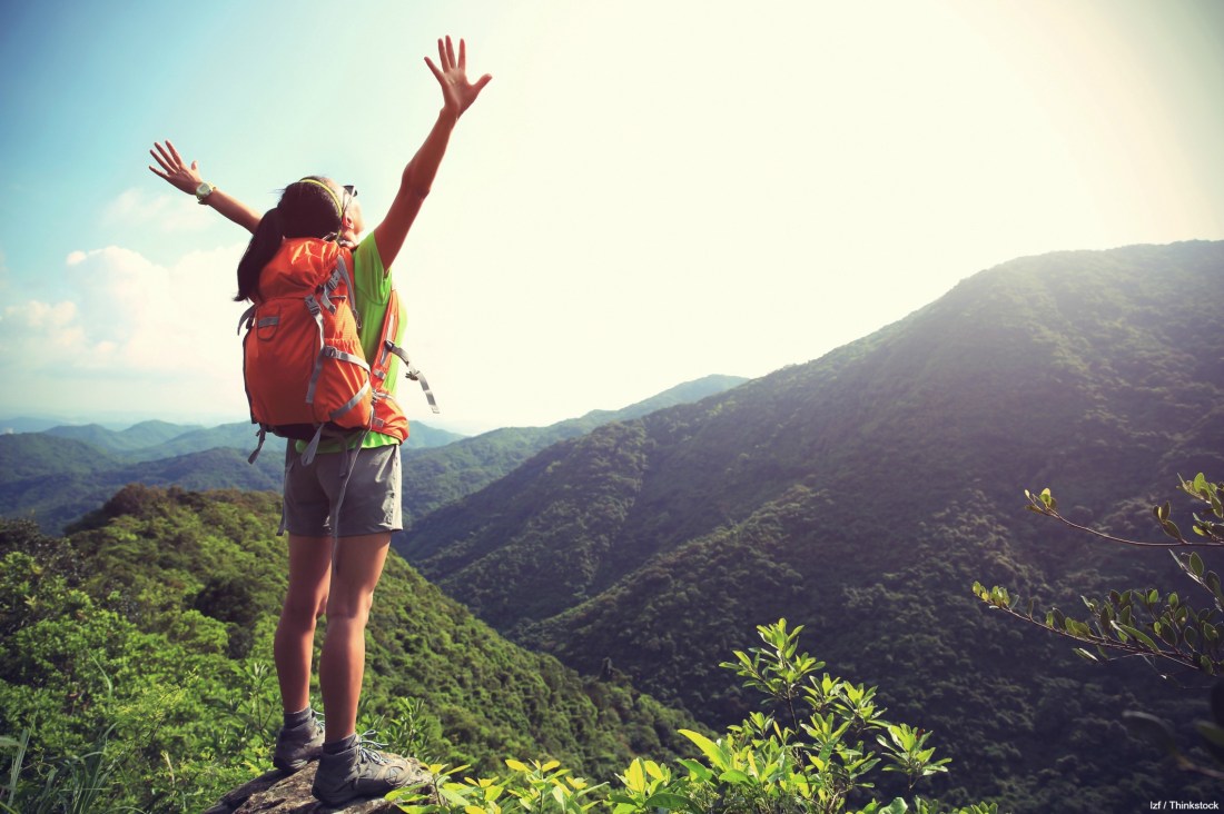cheering young woman hiker open arms at mountain peak